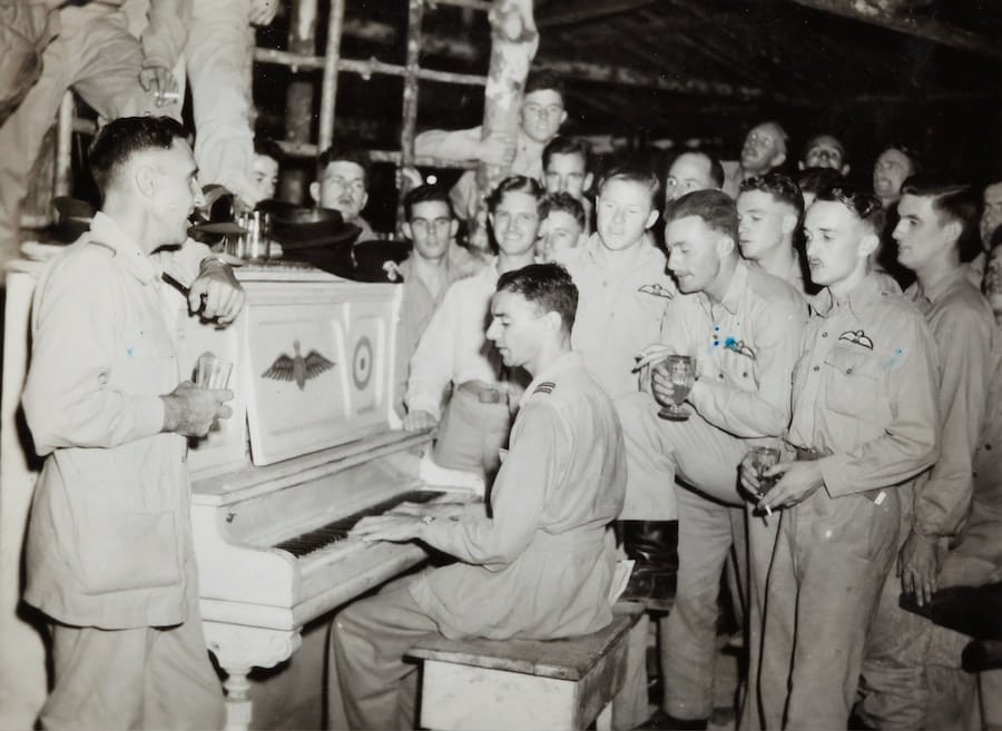 Soldater sjunger runt piano, historiskt fotografi.