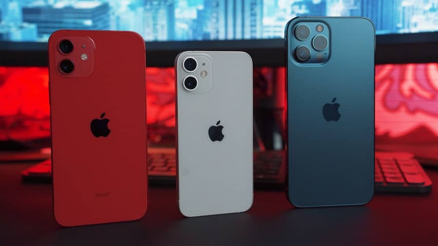 Tre smartphones av olika färger framför datorskärmar.