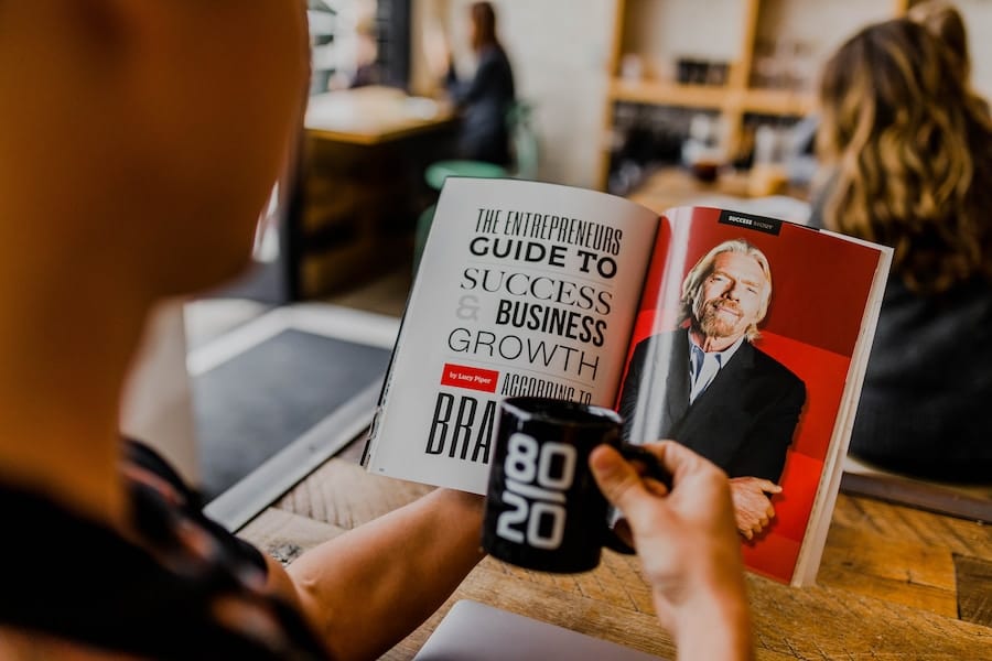 Person läser entreprenörsmagasin i kafémiljö.