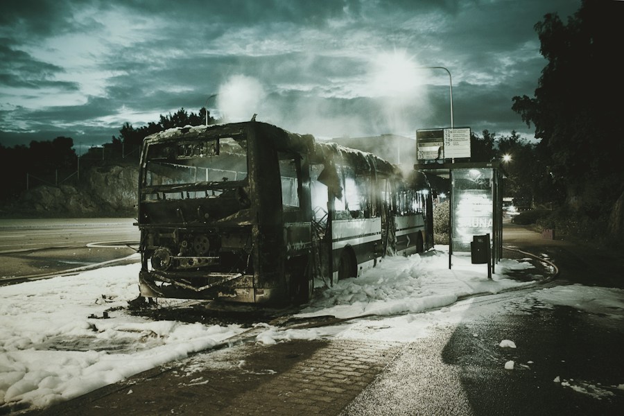 Förstörd buss vid hållplats nattetid.