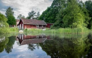 Röd stuga vid spegelblank sjö i Sverige.