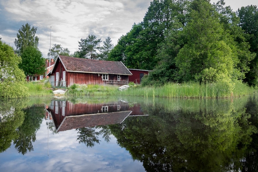 Röd stuga vid spegelblank sjö i Sverige.