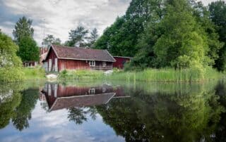 Röd stuga speglas i en lugn sjö.